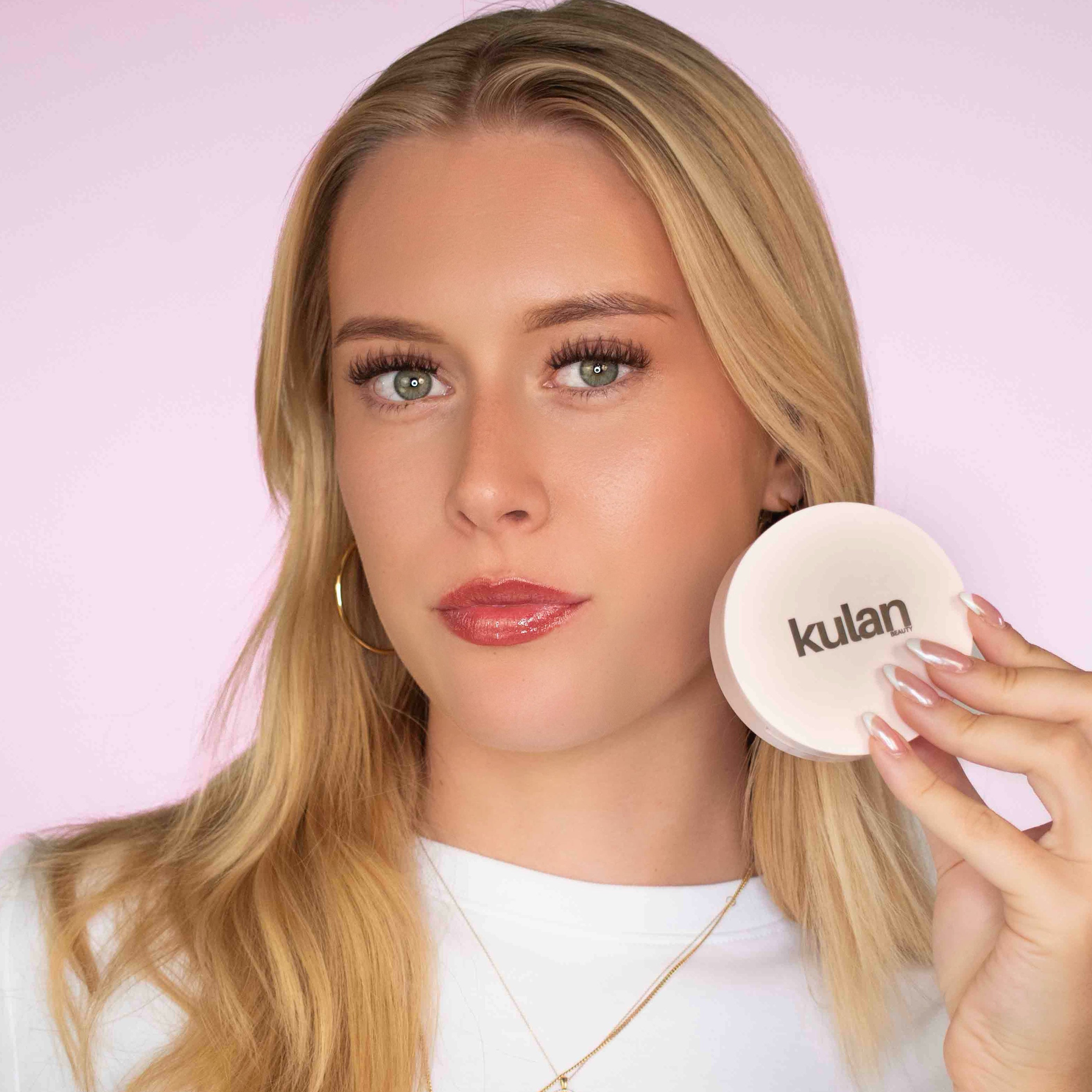 Woman holding a compact mirror with 'kulan' branding against a pink background