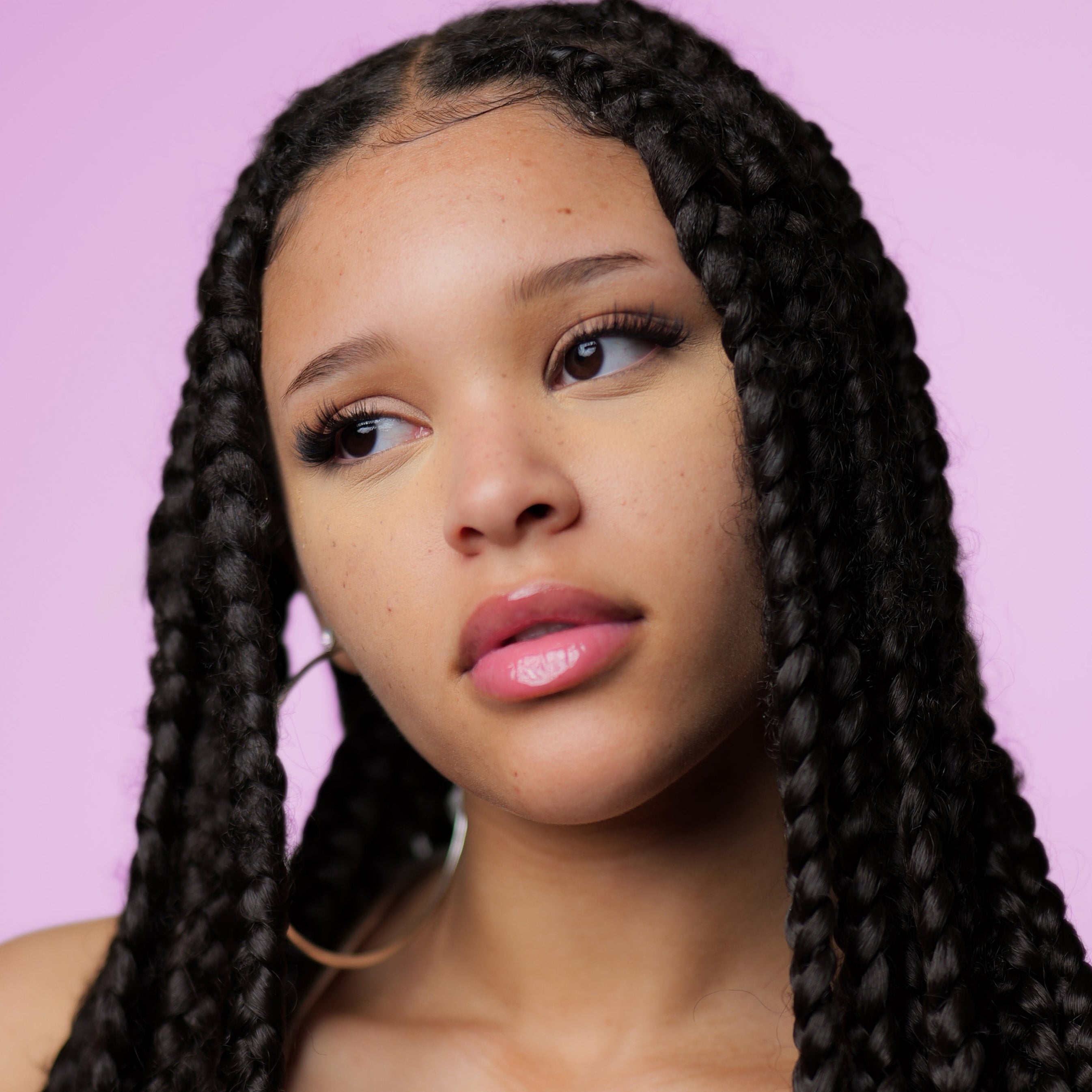 Woman with long braided hair against a pink background